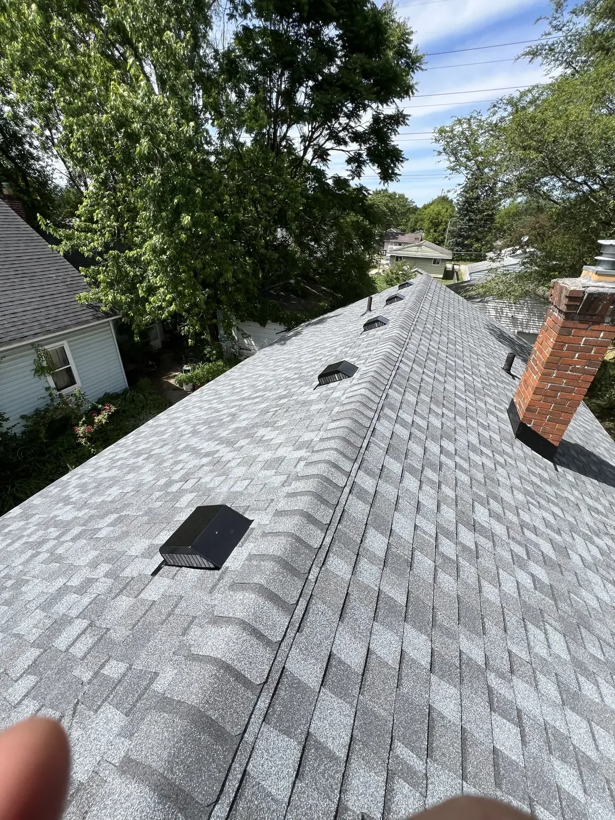 A gray architectural shingle roof with ridge vents and a brick chimney