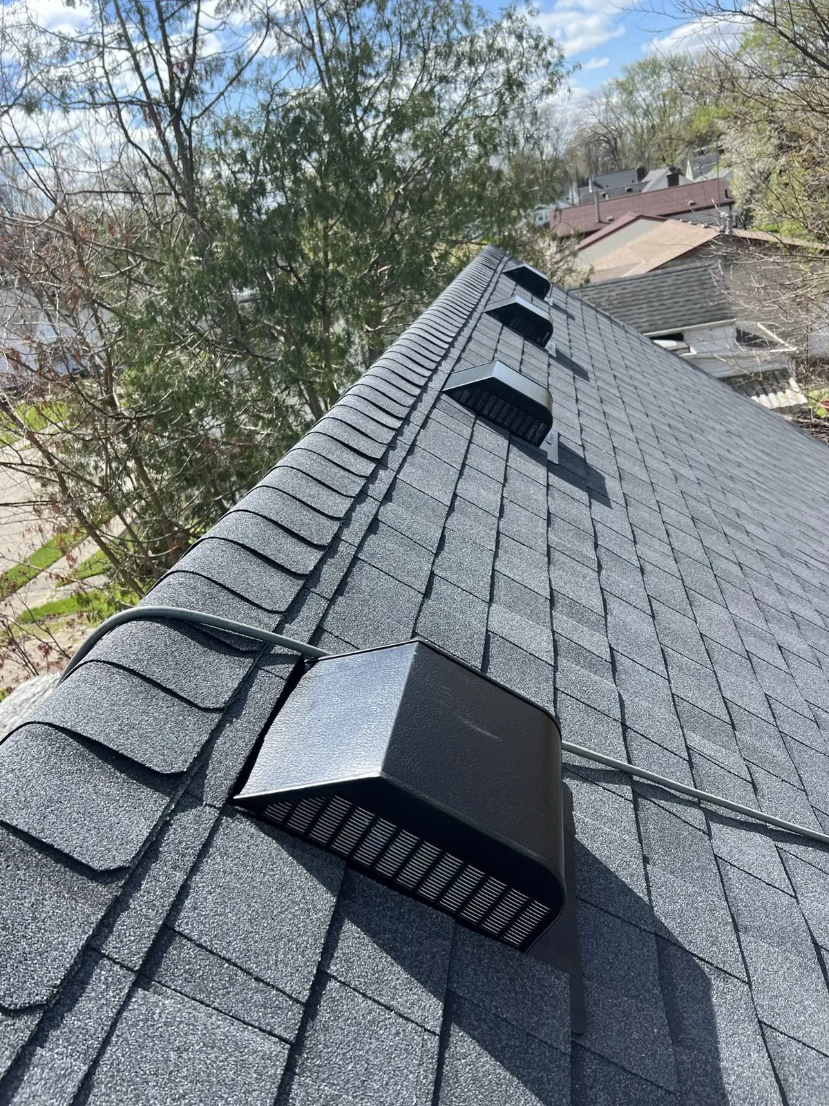 Close view of new black roof vents installed along the ridge of a gray shingle roof